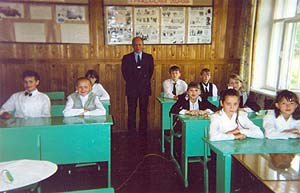 Седьмой класс сидит за двумя рядами парт, между ними у стены, покрытой досками, стоит классный руководитель, как всегда, в черном костюме с галстуком