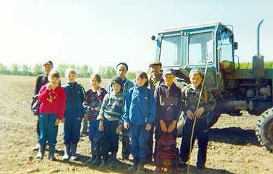 Пятый класс стоит на вспаханном поле рядом с трактором Белорус. С ними Олег и Беляев Валерий